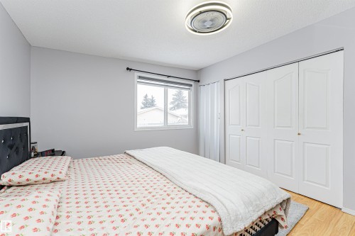 Light gray walls complement the wood-finish flooring in this room featuring a window with blinds, a bi-fold closet, and a ceiling-mounted light fixture - 10412 39 Avenue, Edmonton, AB - Indoor Photo Showing Bedroom
