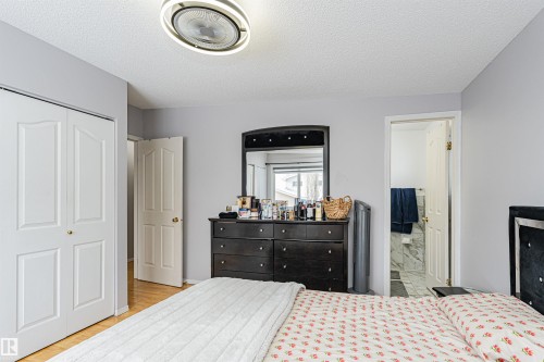 Light gray wall paint with white trim, wood-finish flooring, bi-fold closet doors, ceiling light fixture, and an open doorway revealing a bathroom with marble-patterned wall tile - 10412 39 Avenue, Edmonton, AB - Indoor Photo Showing Bedroom