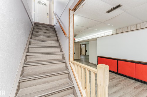 Staircase with wood-finish treads and risers, complemented by a natural wood handrail and newel post - 10412 39 Avenue, Edmonton, AB - Indoor Photo Showing Other Room