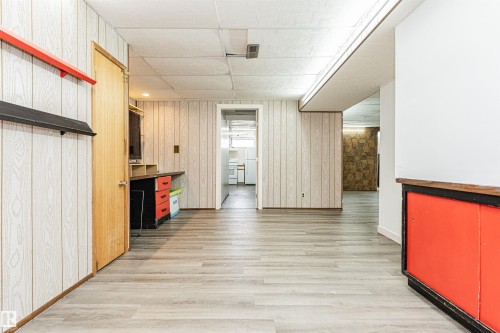 Spacious interior featuring wood-finish flooring, light-toned vertical wall paneling, and an open doorway - 10412 39 Avenue, Edmonton, AB - Indoor Photo Showing Other Room