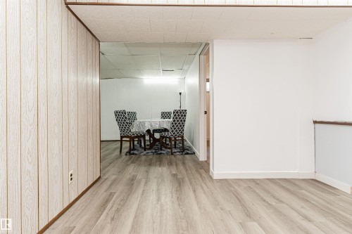 Light wood-finish flooring extends throughout this expansive area, complemented by white painted walls and a wood-paneled accent wall - 10412 39 Avenue, Edmonton, AB - Indoor Photo Showing Other Room