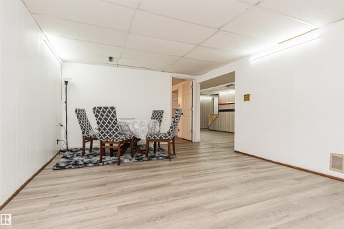 Spacious lower-level room featuring light wood-finish flooring, white paneling, and a drop ceiling with integrated lighting - 10412 39 Avenue, Edmonton, AB - Indoor Photo Showing Other Room