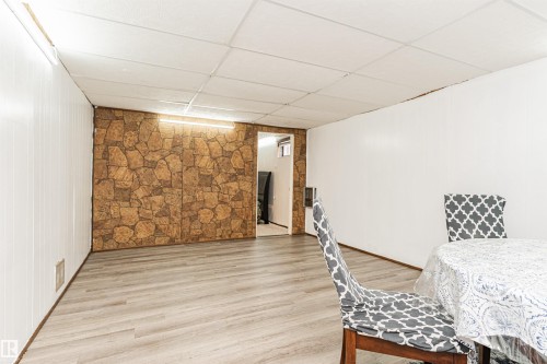 Room featuring wood-finish flooring, white paneling, and a stone-patterned accent wall - 10412 39 Avenue, Edmonton, AB - Indoor