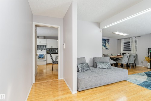 Light wood-finish flooring extends through the entryway and into the kitchen, which features white cabinetry, white appliances, and a black and white tiled backsplash - 10412 39 Avenue, Edmonton, AB - Indoor Photo Showing Other Room