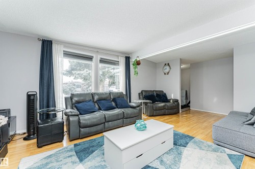 Bright living area featuring wood-finish flooring, light grey walls, and large window openings with white trim - 10412 39 Avenue, Edmonton, AB - Indoor Photo Showing Living Room