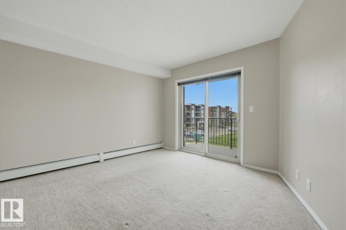 Carpeted room featuring a sliding glass patio door with a black metal railing balcony - 303 11804 22 Avenue, Edmonton, AB - Indoor Photo Showing Other Room