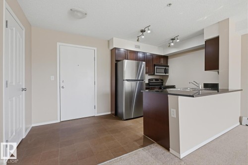 Kitchen area featuring dark wood-finish cabinetry, stainless steel appliances, and a dark countertop breakfast bar - 303 11804 22 Avenue, Edmonton, AB - Indoor Photo Showing Kitchen