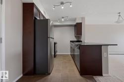 Kitchen featuring dark wood-finish cabinetry, stainless steel appliances, dark countertops, and track lighting - 