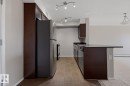 Kitchen featuring dark wood-finish cabinetry, stainless steel appliances, dark countertops, and track lighting - 303 11804 22 Avenue, Edmonton, AB  - Indoor Photo Showing Kitchen 