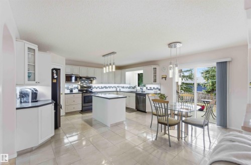 The kitchen features white cabinetry, black countertops, and a central island - #1 Colonial Close, Beaumont, AB - Indoor