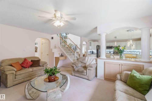 The Family room features carpeted flooring and a ceiling fan, with a view of the kitchen showcasing white cabinetry and pendant lighting - #1 Colonial Close, Beaumont, AB - Indoor Photo Showing Living Room