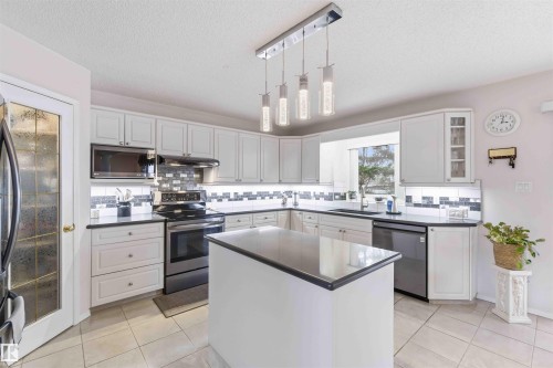 The kitchen features ample white cabinetry, a central island with a contrasting countertop, and stainless steel appliances - #1 Colonial Close, Beaumont, AB - Indoor Photo Showing Kitchen