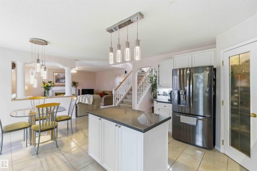 The kitchen features an island with a dark countertop, white cabinetry, and a modern pendant light fixture - #1 Colonial Close, Beaumont, AB - Indoor Photo Showing Other Room