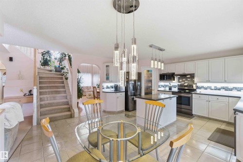 Spacious open-concept kitchen featuring white cabinetry, a kitchen island with dark countertops, stainless steel appliances, and a tiled backsplash - #1 Colonial Close, Beaumont, AB - Indoor Photo Showing Kitchen With Stainless Steel Kitchen