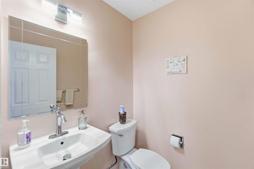 The bathroom features a pedestal sink with a chrome faucet, a wall-mounted mirror, and a toilet - #1 Colonial Close, Beaumont, AB - Indoor Photo Showing Bathroom