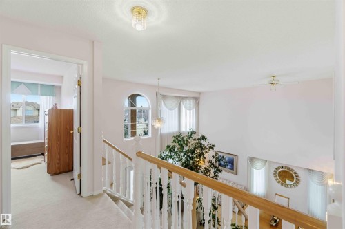 The property features a staircase with white balusters and a light wood handrail, leading to a landing with a light-colored carpet - #1 Colonial Close, Beaumont, AB - Indoor Photo Showing Other Room