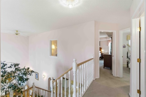 The property features a staircase with white railings, a carpeted hallway, and an entryway with a light-colored door - #1 Colonial Close, Beaumont, AB - Indoor Photo Showing Other Room