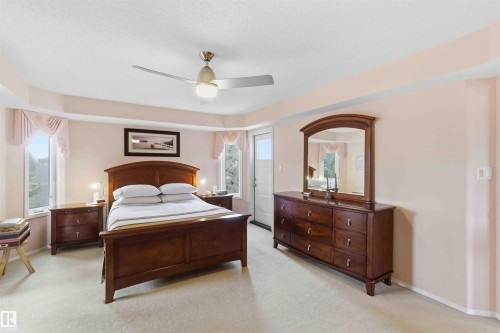 The property features a bedroom with light-colored walls and carpeting, a ceiling fan with integrated lighting, and multiple windows - #1 Colonial Close, Beaumont, AB - Indoor Photo Showing Bedroom