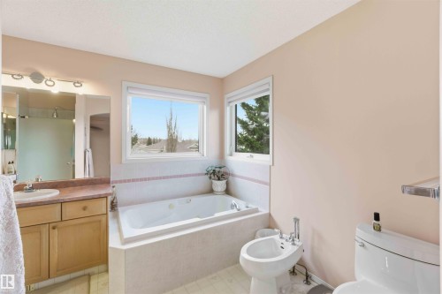 The bathroom features a built-in bathtub, a window providing natural light, a vanity with a sink and mirror, and a toilet with a bidet - #1 Colonial Close, Beaumont, AB - Indoor Photo Showing Bathroom
