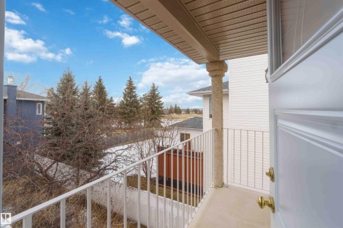 The property features a balcony with a white metal railing, an ornate stone column, and an exterior door with brass hardware - #1 Colonial Close, Beaumont, AB - Outdoor With Balcony With Exterior