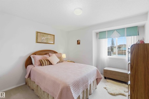 This room features neutral walls, carpeted flooring, and a window with a view of residential rooftops - #1 Colonial Close, Beaumont, AB - Indoor Photo Showing Bedroom