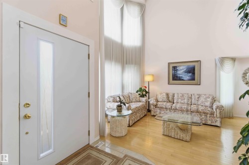 The entrance features a white door with a vertical glass panel and brass hardware, opening to a living area with light-toned hardwood flooring - #1 Colonial Close, Beaumont, AB - Indoor Photo Showing Living Room