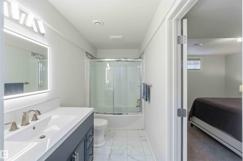 Bathroom featuring a vanity with a white countertop and double basin sink, a lighted mirror, and a bathtub with a sliding glass door - #1 Colonial Close, Beaumont, AB - Indoor Photo Showing Bathroom