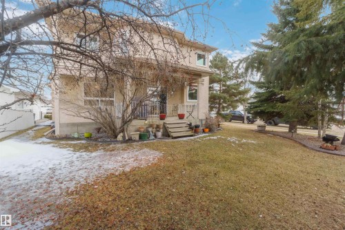 The property features a two-story exterior with a porch, a front yard with a lawn, and mature evergreen trees - #1 Colonial Close, Beaumont, AB - Outdoor