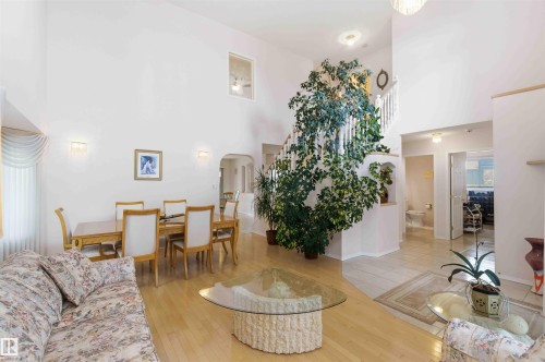 The interior features high ceilings, hardwood flooring, and a staircase with white balusters - #1 Colonial Close, Beaumont, AB - Indoor Photo Showing Living Room