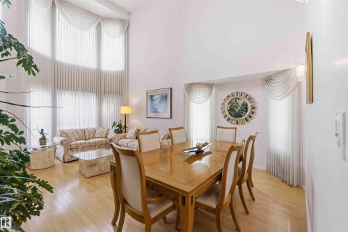 This expansive interior space features high ceilings, hardwood flooring, and large windows with elegant drapes - #1 Colonial Close, Beaumont, AB - Indoor Photo Showing Dining Room