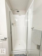 Walk-in shower featuring a white surround, clear glass enclosure, and a chrome shower head with coordinating fixtures - 