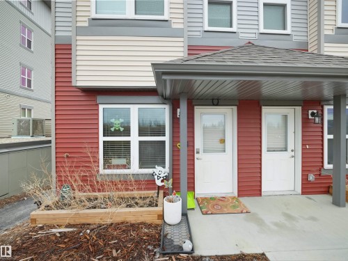 The property features red siding and a covered front entry with white doors - 64 655 Watt Boulevard, Edmonton, AB - Outdoor
