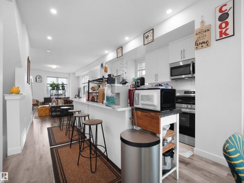 The kitchen features white cabinetry and stainless steel appliances, complemented by a breakfast bar with seating - 64 655 Watt Boulevard, Edmonton, AB - Indoor Photo Showing Other Room