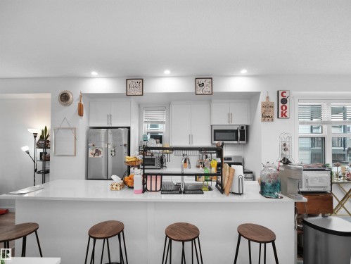 The kitchen features white cabinetry, stainless steel appliances, and a large island with a white countertop - 64 655 Watt Boulevard, Edmonton, AB - Indoor
