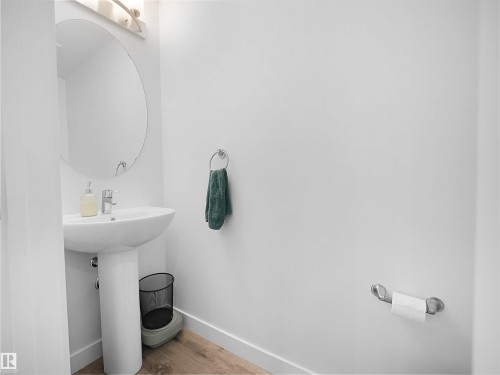 Bathroom featuring a white pedestal sink, a wall-mounted mirror, and wood-look flooring - 64 655 Watt Boulevard, Edmonton, AB - Indoor Photo Showing Bathroom