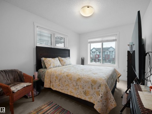 This bedroom features two windows providing natural light, a dark wood headboard, and a ceiling-mounted light fixture - 64 655 Watt Boulevard, Edmonton, AB - Indoor Photo Showing Bedroom