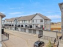 The property is a multi-story townhome featuring a private balcony with black railings, a garage with a roll-up door, and a light-colored exterior with white trim - 64 655 Watt Boulevard, Edmonton, AB  - Outdoor With Exterior 