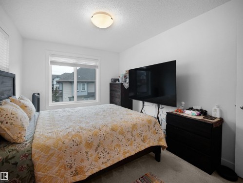 This bedroom features a window providing natural light and views of the surrounding homes, a ceiling light fixture, and light-colored walls - 64 655 Watt Boulevard, Edmonton, AB - Indoor Photo Showing Bedroom
