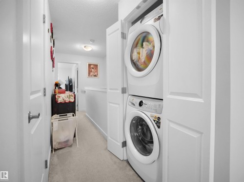 The property includes a laundry area with a stacked washer and dryer, located in a hallway with light-colored carpeting and white walls - 64 655 Watt Boulevard, Edmonton, AB - Indoor Photo Showing Laundry Room
