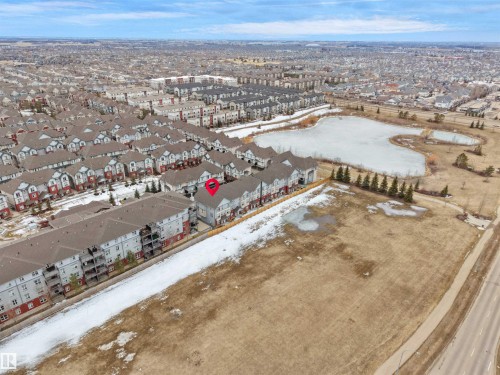 Aerial view showcasing the property within a community of residences, with a frozen pond and mature trees visible in the general vicinity - 64 655 Watt Boulevard, Edmonton, AB - Outdoor With View