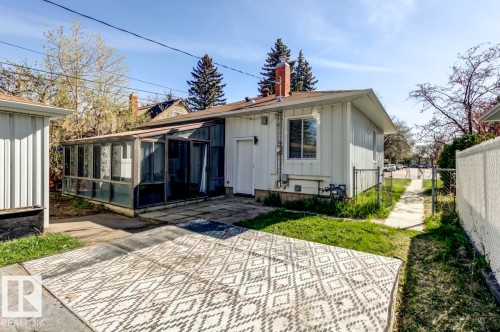 Rear exterior featuring an enclosed sunroom with multiple glass panels, white vertical siding, and a brick chimney - 9602 90 Street, Edmonton, AB - Outdoor