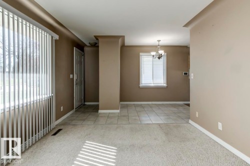 Open-concept living space featuring neutral carpet flooring, a large window with vertical blinds, and a tiled entryway - 9602 90 Street, Edmonton, AB - Indoor Photo Showing Other Room