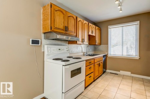 Kitchen featuring wood cabinetry, white appliances, tile flooring, and a window with blinds - 9602 90 Street, Edmonton, AB - Indoor Photo Showing Kitchen With Double Sink