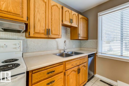 Kitchen featuring wood cabinetry, a double basin stainless steel sink, a tile backsplash, and a white electric range - 9602 90 Street, Edmonton, AB - Indoor Photo Showing Kitchen With Double Sink