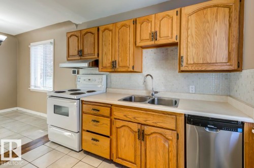 Kitchen featuring wood cabinetry, white countertops, a double basin stainless steel sink, a stainless steel dishwasher, and a white electric range with an overhead exhaust fan - 9602 90 Street, Edmonton, AB - Indoor Photo Showing Kitchen With Double Sink