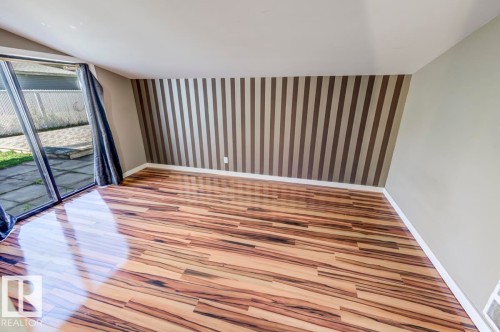 Spacious room featuring wood-finish flooring, a full-height striped accent wall, and light-toned painted walls - 9602 90 Street, Edmonton, AB - Indoor Photo Showing Other Room