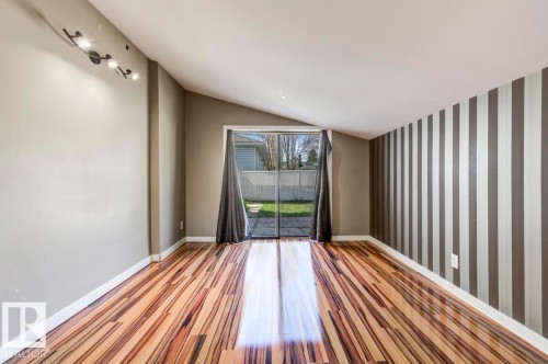 Sliding glass door leading to the outdoor space, featuring warm wood-finish flooring, a vaulted ceiling, and track lighting - 9602 90 Street, Edmonton, AB - Indoor Photo Showing Other Room