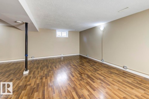Expansive room featuring wood-finish flooring, neutral-toned walls, and a textured ceiling - 9602 90 Street, Edmonton, AB - Indoor