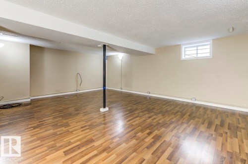 Spacious room featuring wood-finish flooring, neutral-toned walls, a textured ceiling, and a secure window - 9602 90 Street, Edmonton, AB - Indoor