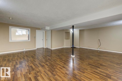 Spacious room featuring wood-finish flooring, neutral-toned walls, a window with white trim, and a white interior door - 9602 90 Street, Edmonton, AB - Indoor Photo Showing Other Room